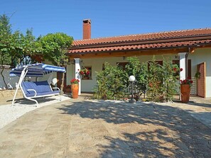 A villa with a tiled roof, a patio with a lounge chair, potted plants, and a lamp post. - Apartment 1770 (Kanfanar)