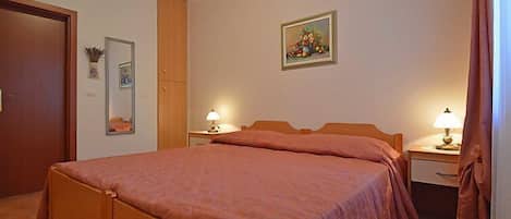 A bedroom with a wooden bed, two bedside tables with lamps, a door, a mirror, and a framed picture on the wall.