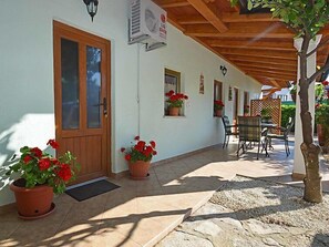 A covered outdoor area with a wooden door, potted red flowers, and a table with chairs. - Apartment 1770 (Kanfanar)