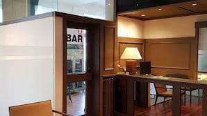 A modern hotel room with a wooden floor, a desk with a lamp, a chair, and a view of the bar area. - Hotel Terminus Puigcerdà (Puigcerda)