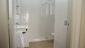 A bathroom with white tiles, a shower, a toilet, and a sink.