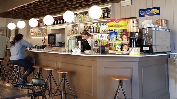 A bar area with stools, a counter, and a person working behind it. - Hotel Terminus Puigcerdà (Puigcerda)