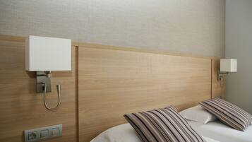 Habitación de hotel con cabecera de madera, dos lámparas de noche, un enchufe y almohadas a rayas.
