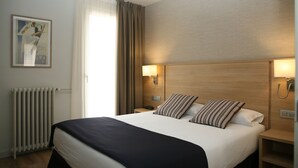 A hotel room with a large bed, two bedside tables, a nightstand, a wall-mounted lamp, a radiator, and a framed picture on the wall. - Hotel Terminus Puigcerdà (Puigcerda)