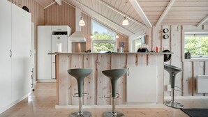 Eine moderne Küche mit Holzelementen, eine zentrale Kochinsel mit Barhocker und ein großes Fenster für natürliches Licht.