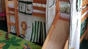 Un área de juegos infantiles con una cama litera, una casita y un mural en la pared.