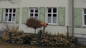 Un edificio de dos pisos con contraventanas verdes, techo triangular y una chimenea visible.