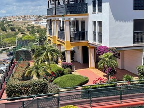 A multi-story residential building with balconies, a landscaped garden, and a view of a hilly town. - "Apartamento Puesta de Sol", Golf, Piscinas. Playas en Costa de la Luz y Algarve (Ayamonte)