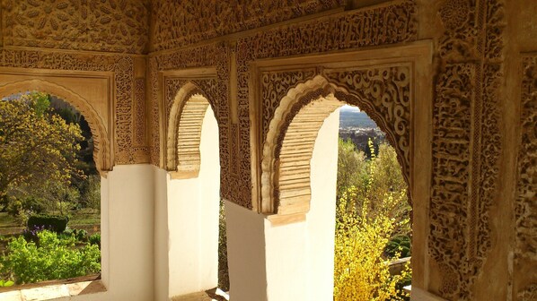 An interior with ornate arches and detailed carvings, leading to a view of a garden and distant landscape.