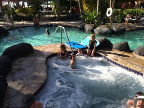 Ein Whirlpoolbereich mit spielenden Kindern, umgeben von Felsen und einem Schwimmbecken.