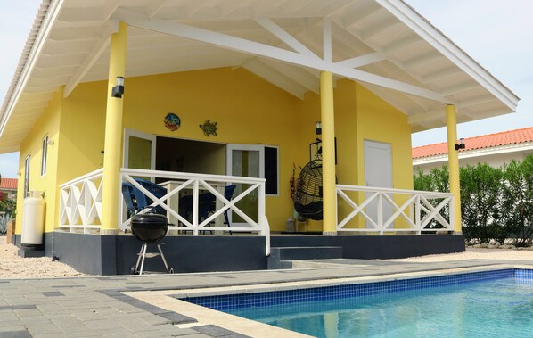 Un edificio amarillo con un porche cubierto, piscina y parrilla.