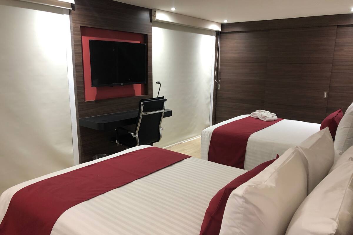 Une chambre d’hôtel avec deux lits, une télévision, un bureau et une douche.