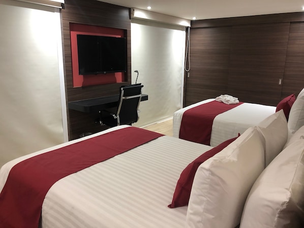 Habitación de hotel con dos camas, televisión, escritorio y ducha.