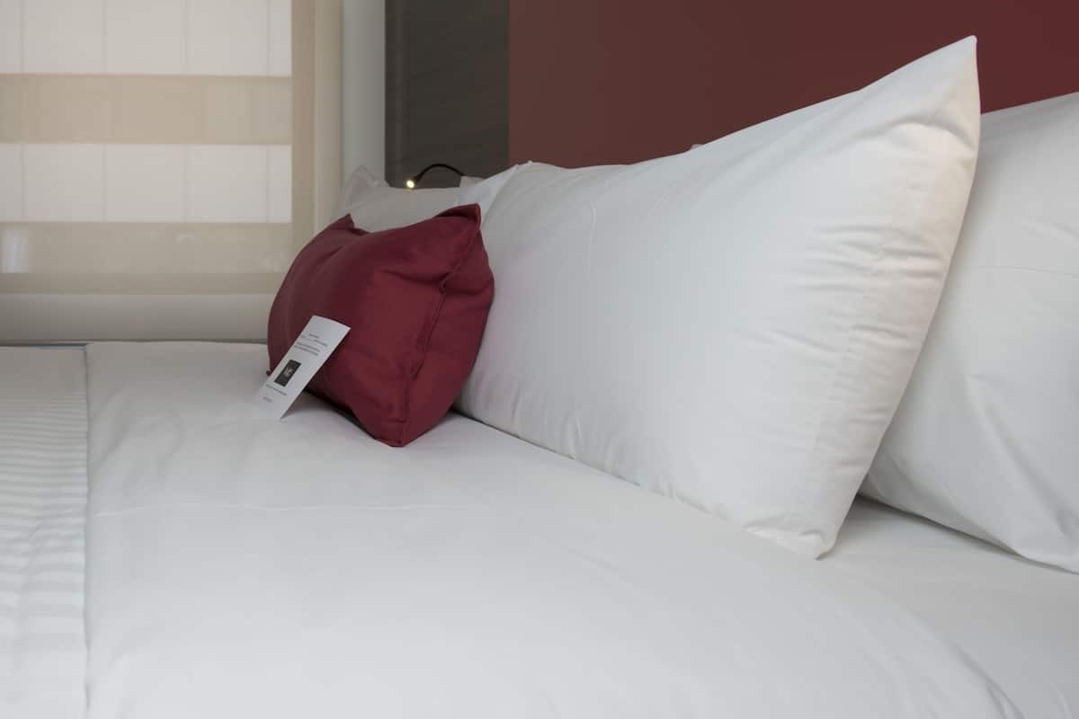 Un lit avec une literie blanche et un oreiller rouge.