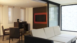 Ein modernes Wohnzimmer mit Sofa, einem an der Wand befestigten Fernseher und einem Essbereich mit Tisch und Stühlen.