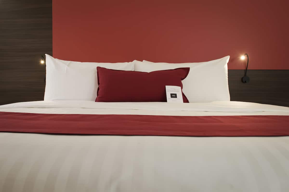 Un lit bien fait, avec une literie blanche et rouge, un oreiller rouge et une petite table de chevet avec une lampe.
