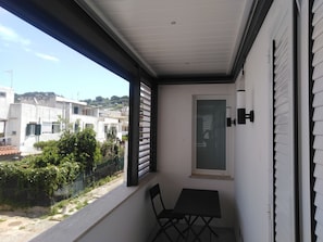 A balcony with a table and chairs, a window with a view of buildings, and a door with a light fixture. - Il Monacone (Capri)
