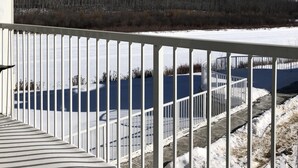 Lumipeitteinen terassi, jossa on kaide, ja josta avautuu näkymä metsäiselle kukkulalle ja vesistölle.