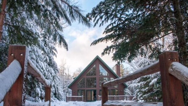 Een lodge met een opvallend driehoekig dak en grote ramen, omringd door met sneeuw bedekte bomen.