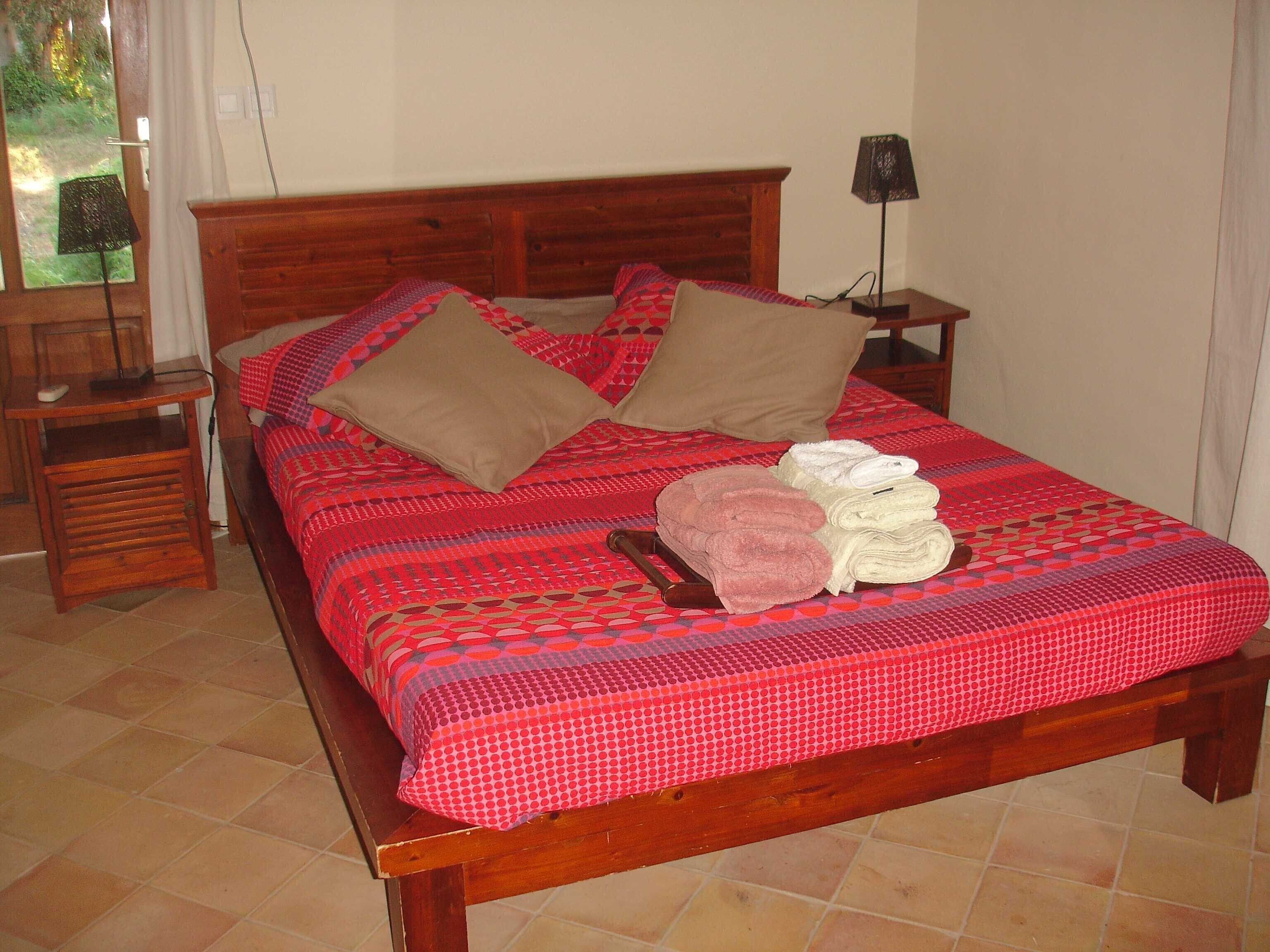 Una cama bien hecha con un edredón estampado, dos almohadas y una pila de toallas dobladas.