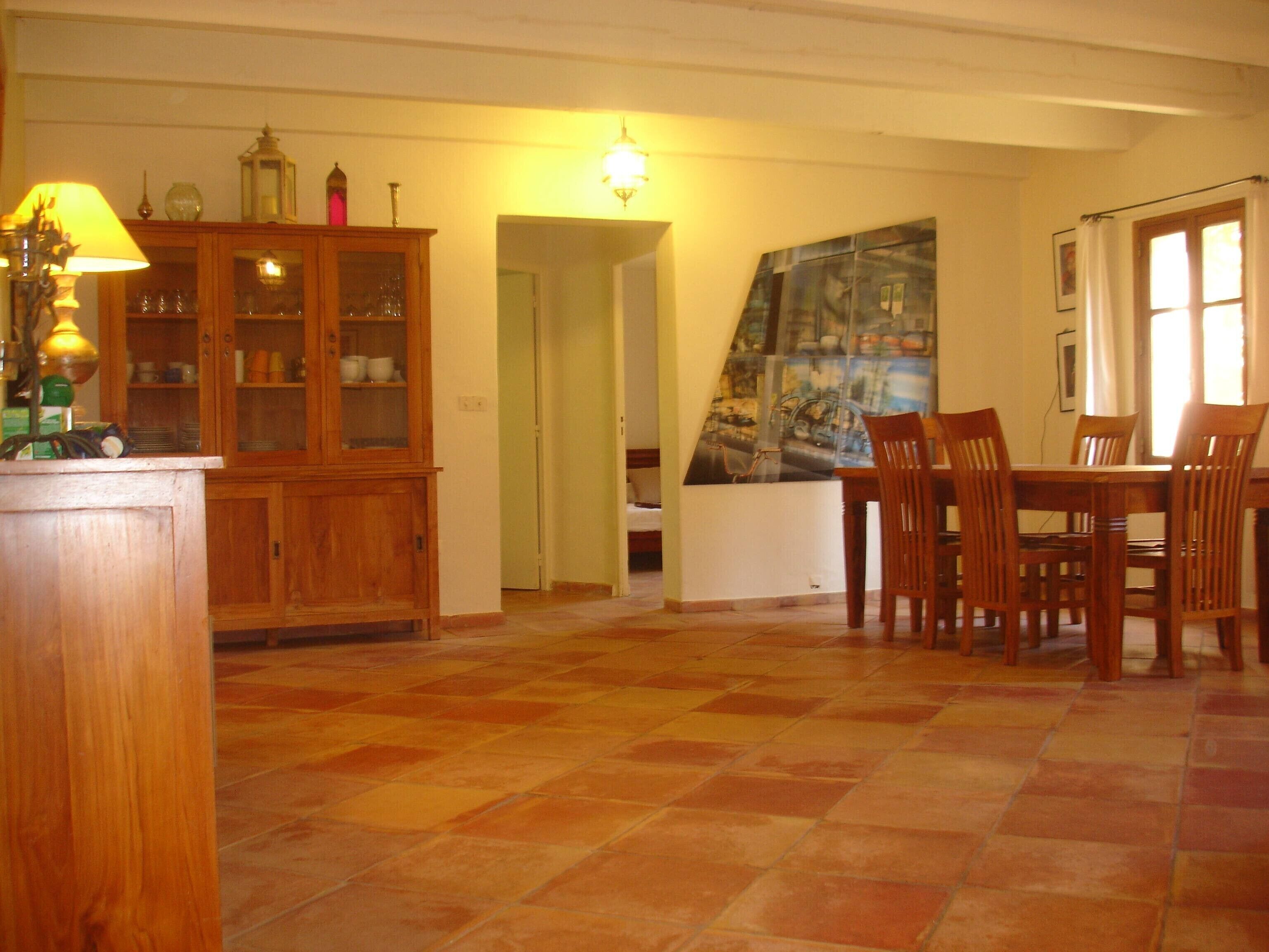 A dining area with a wooden table and chairs, a cabinet with glass doors, and a tiled floor.