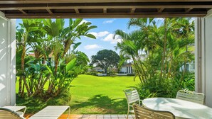 A patio with a table and chairs, a lawn, and tropical plants.