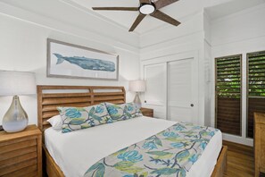 A bedroom with a wooden headboard, a bed with floral bedding, a wall-mounted artwork of a whale, and a ceiling fan. - Rare find w/ 2 AC, 2 min walk to beach, Remodeled #151, ground floor!  (Koloa)