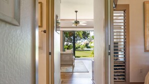 A hallway with wooden flooring, a ceiling fan, and a view of a garden through an open door.