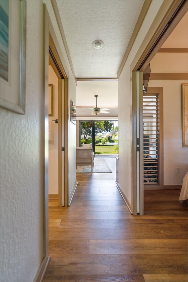 Un couloir doté d’un plancher en bois, d’un ventilateur de plafond et offrant une vue sur un jardin par une porte ouverte.