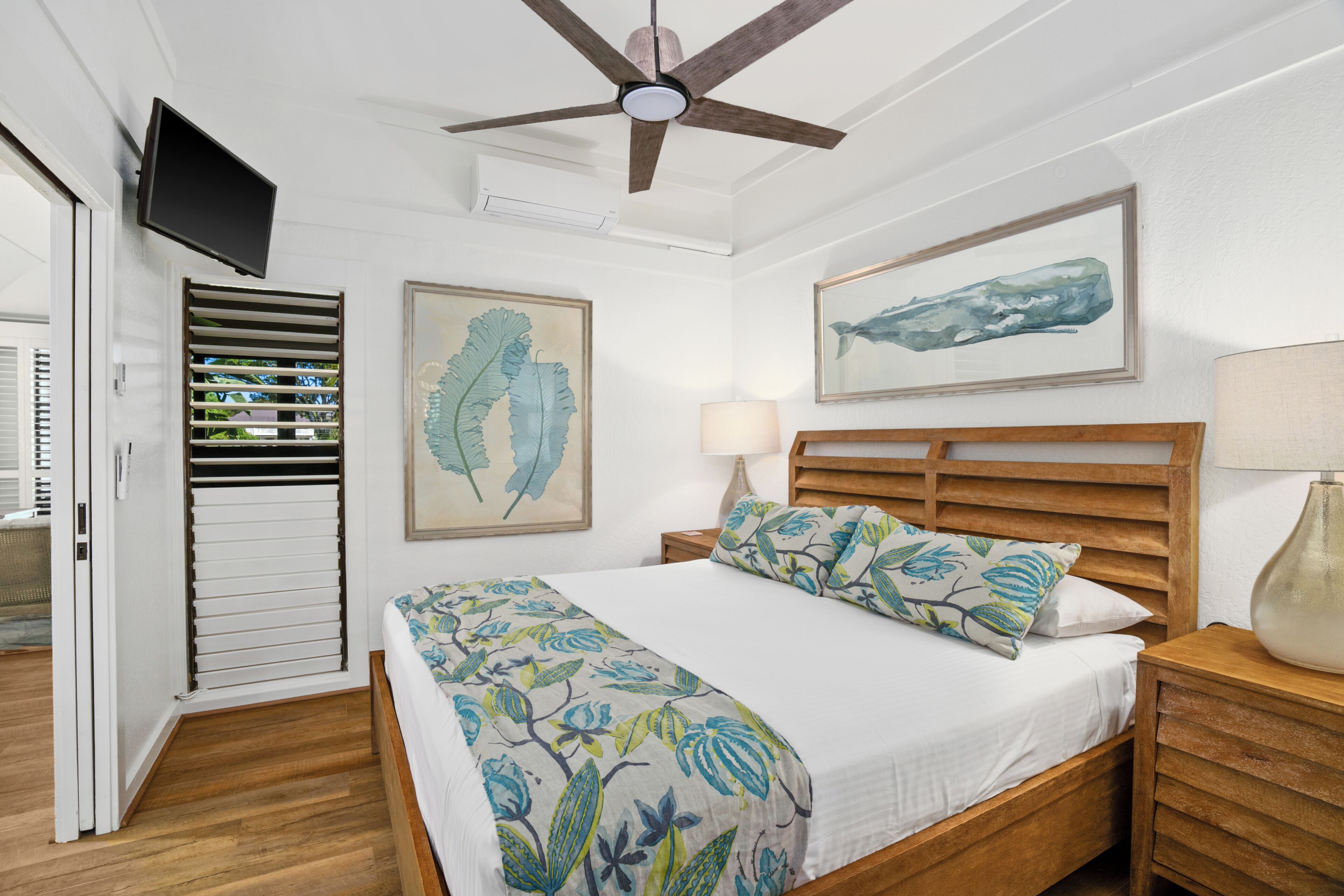A bedroom with a bed, a ceiling fan, a mounted TV, and artwork on the walls.