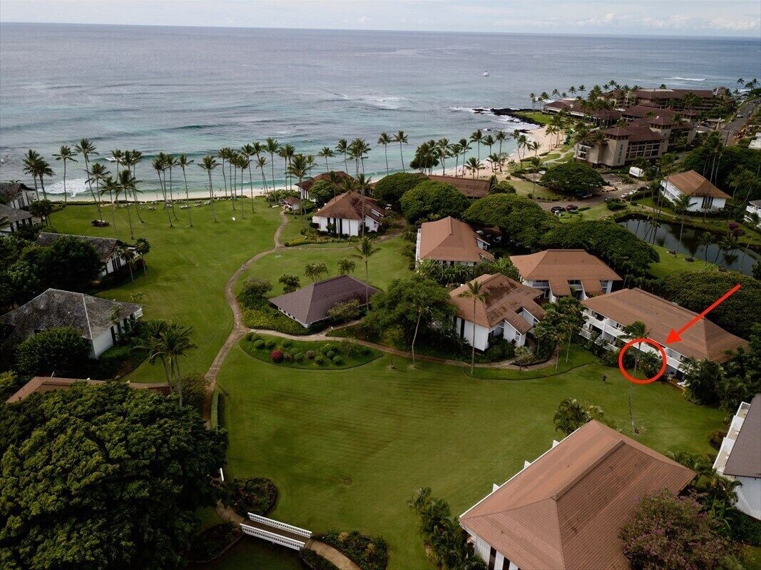 An aerial view of a coastal residential area with houses, a golf course, and a beach.