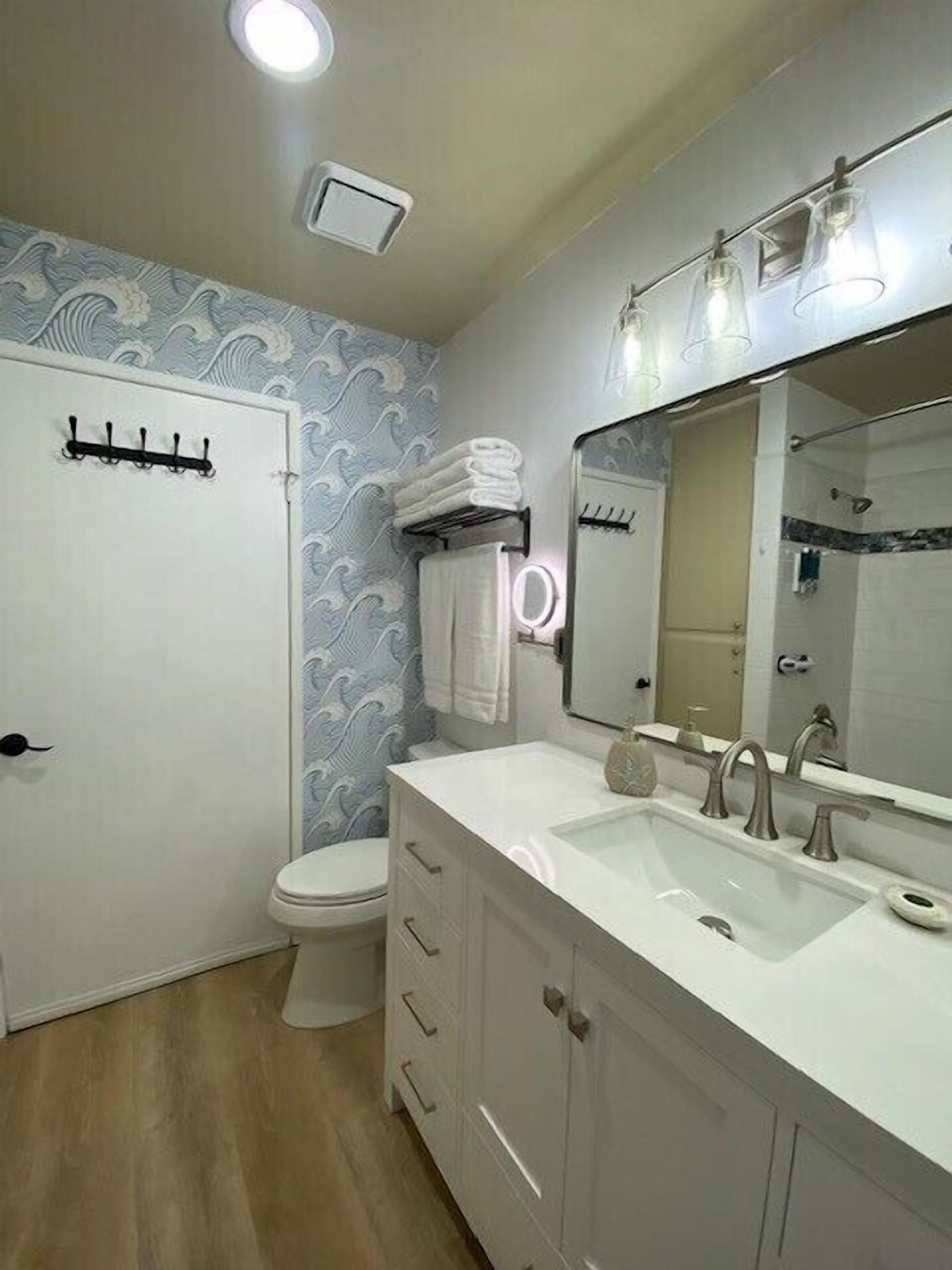 Un baño con inodoro blanco, lavamanos con espejo y un perchero para toallas.