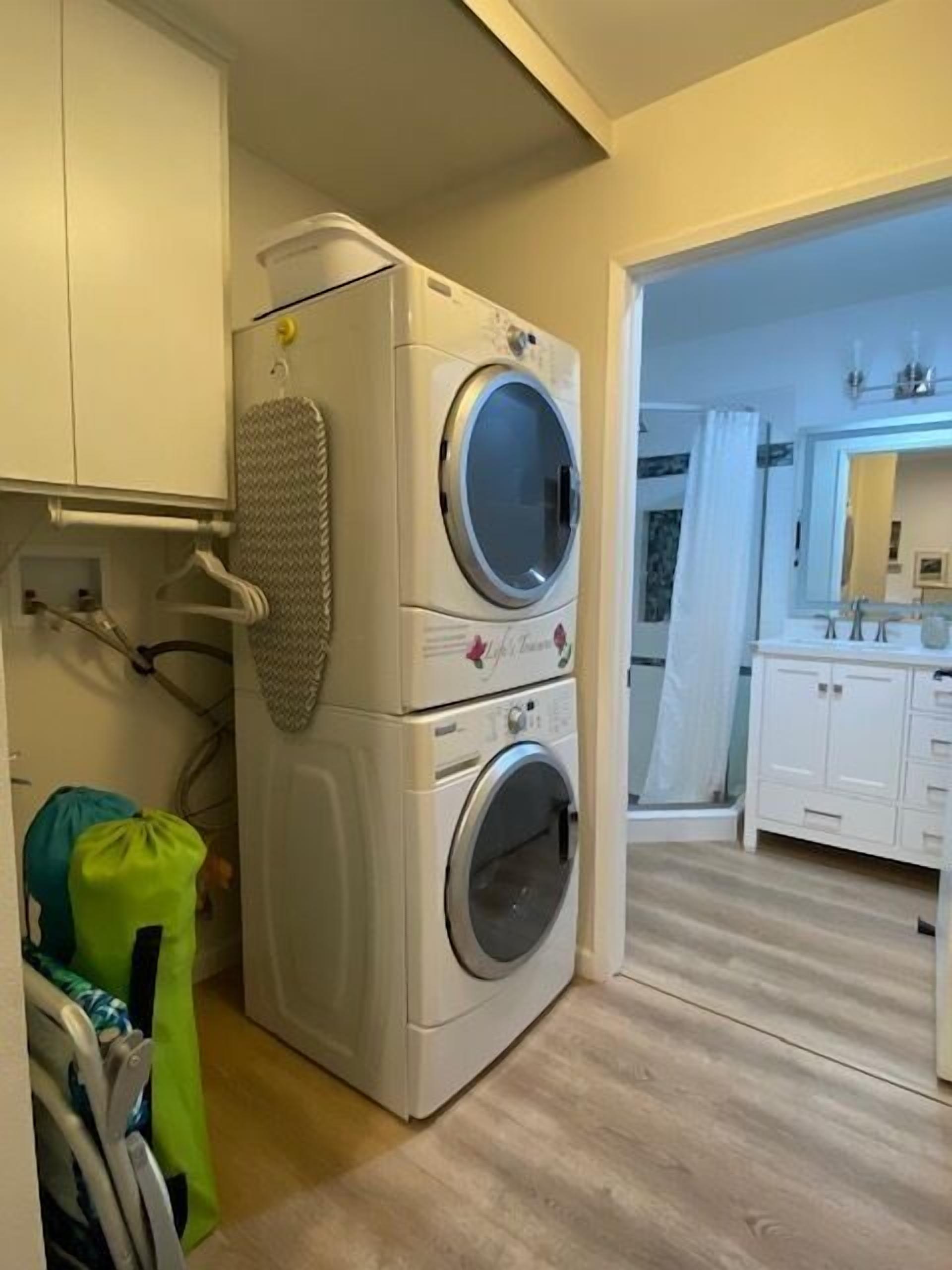 A laundry area with a stacked washer and dryer, a drying rack, and a green bag.