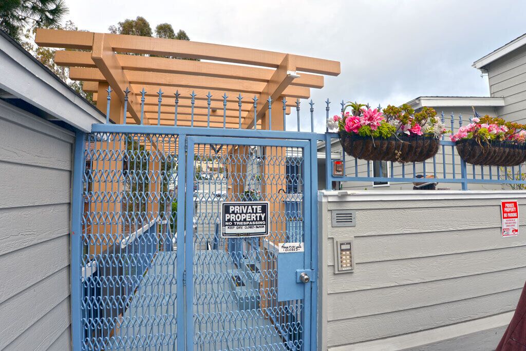 A gated entrance with a blue metal gate, a wooden pergola, and flower planters.