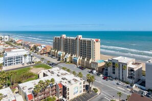 A coastal hotel with multiple floors, a parking lot, and a view of the ocean.