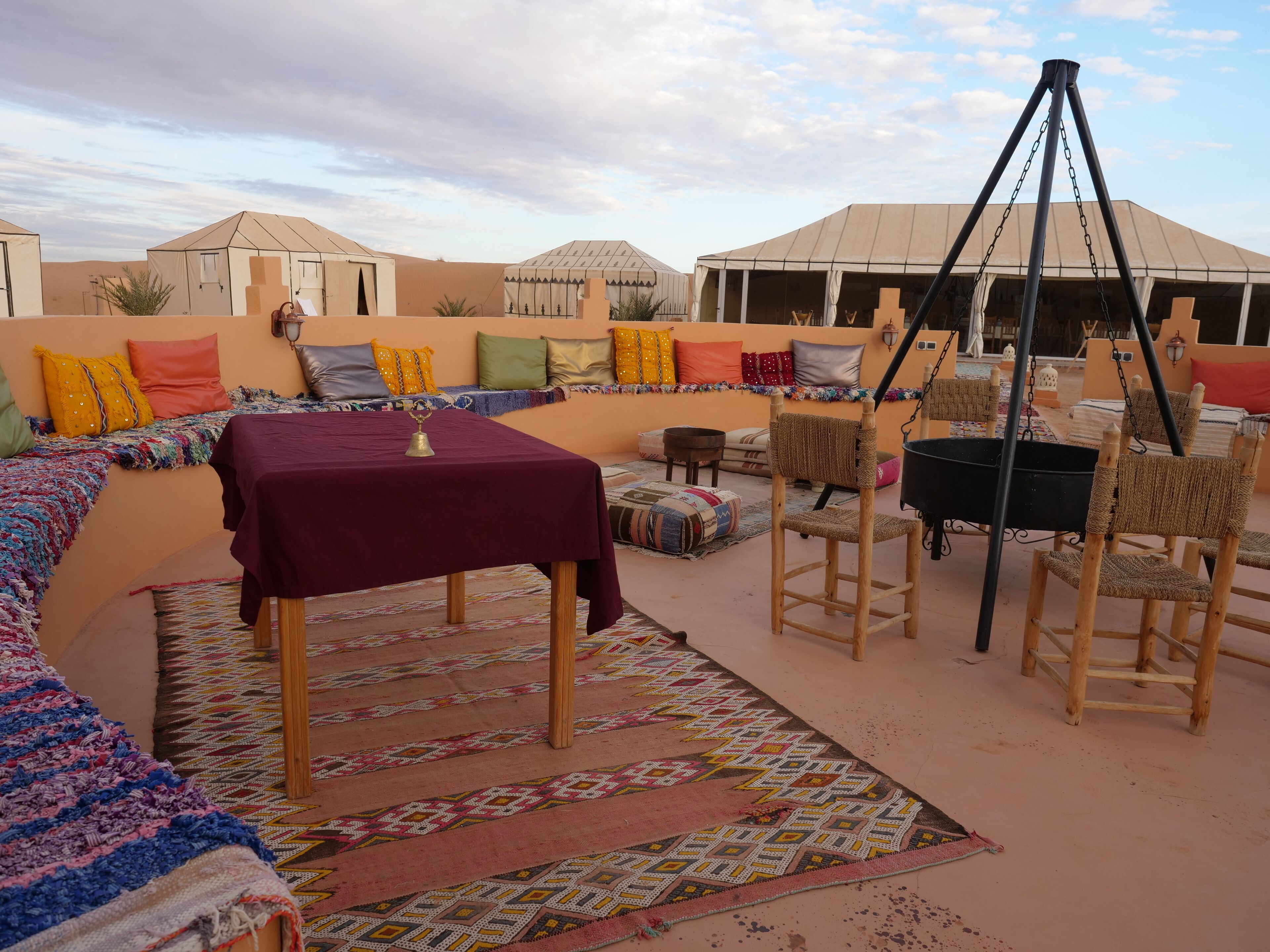 Un rincón exterior acogedor con una mesa y sillas, rodeado de cojines de colores y una alfombra estampada.