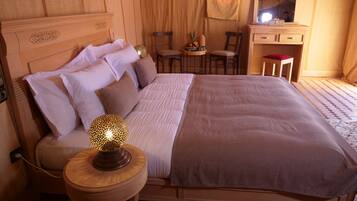 Un dormitorio ordenado con cama, lámparas de noche, una mesita con fruteros, una silla y un espejo.