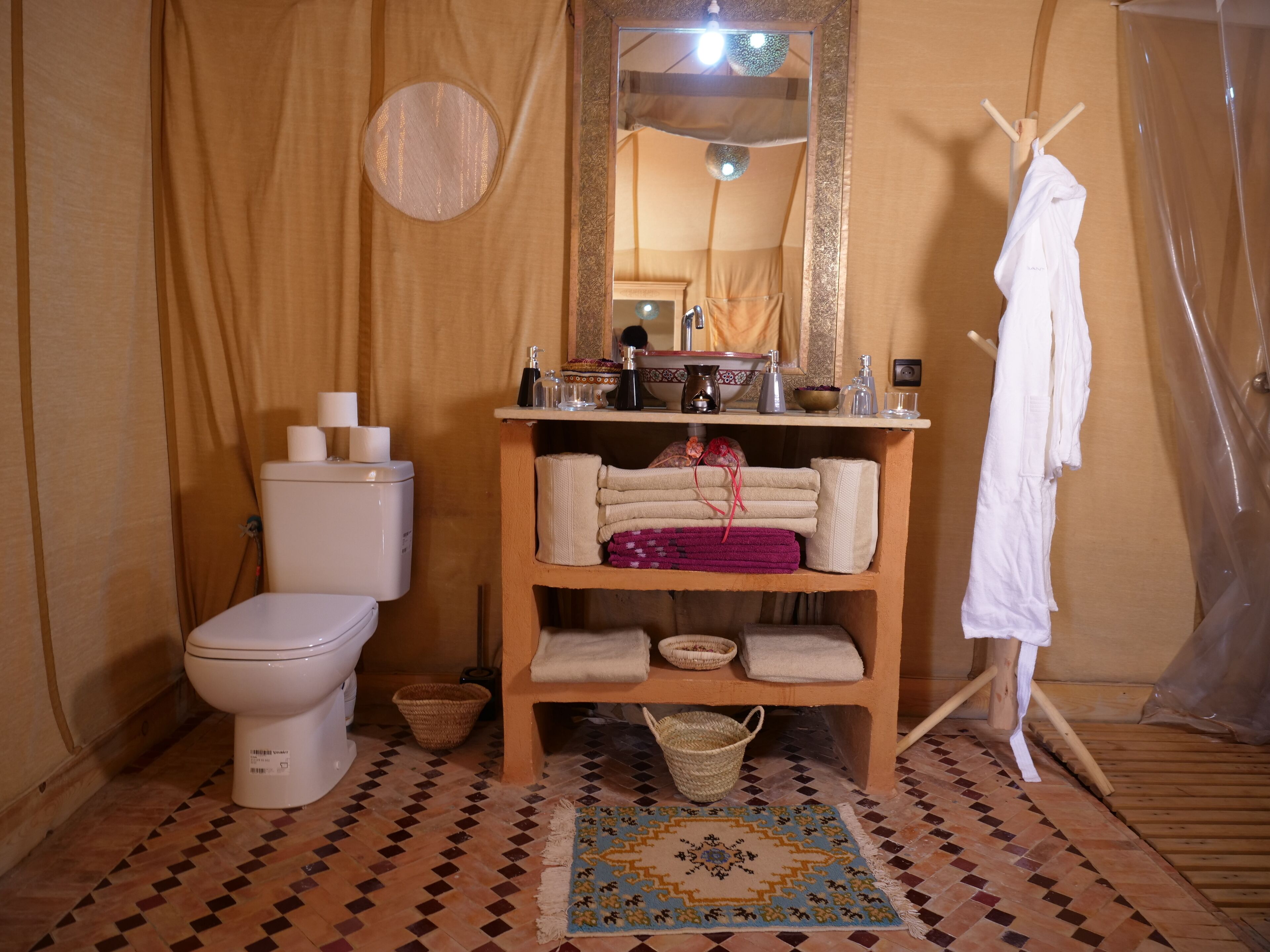 A bathroom with a toilet, sink, and wooden vanity with towels and toiletries.