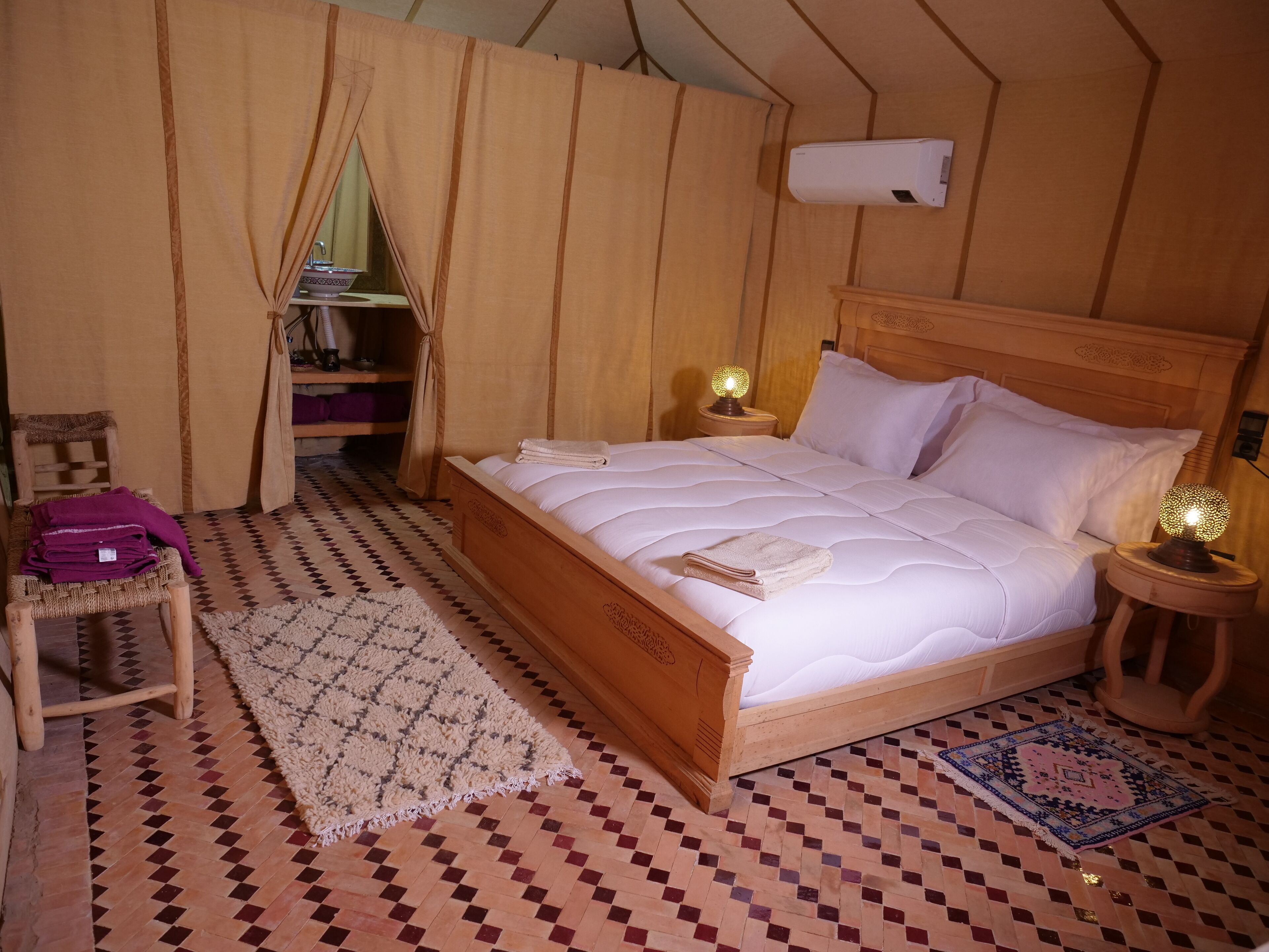 Habitación acogedora con cama de madera, una pequeña silla, una mesita de noche con lámpara y una alfombra estampada.