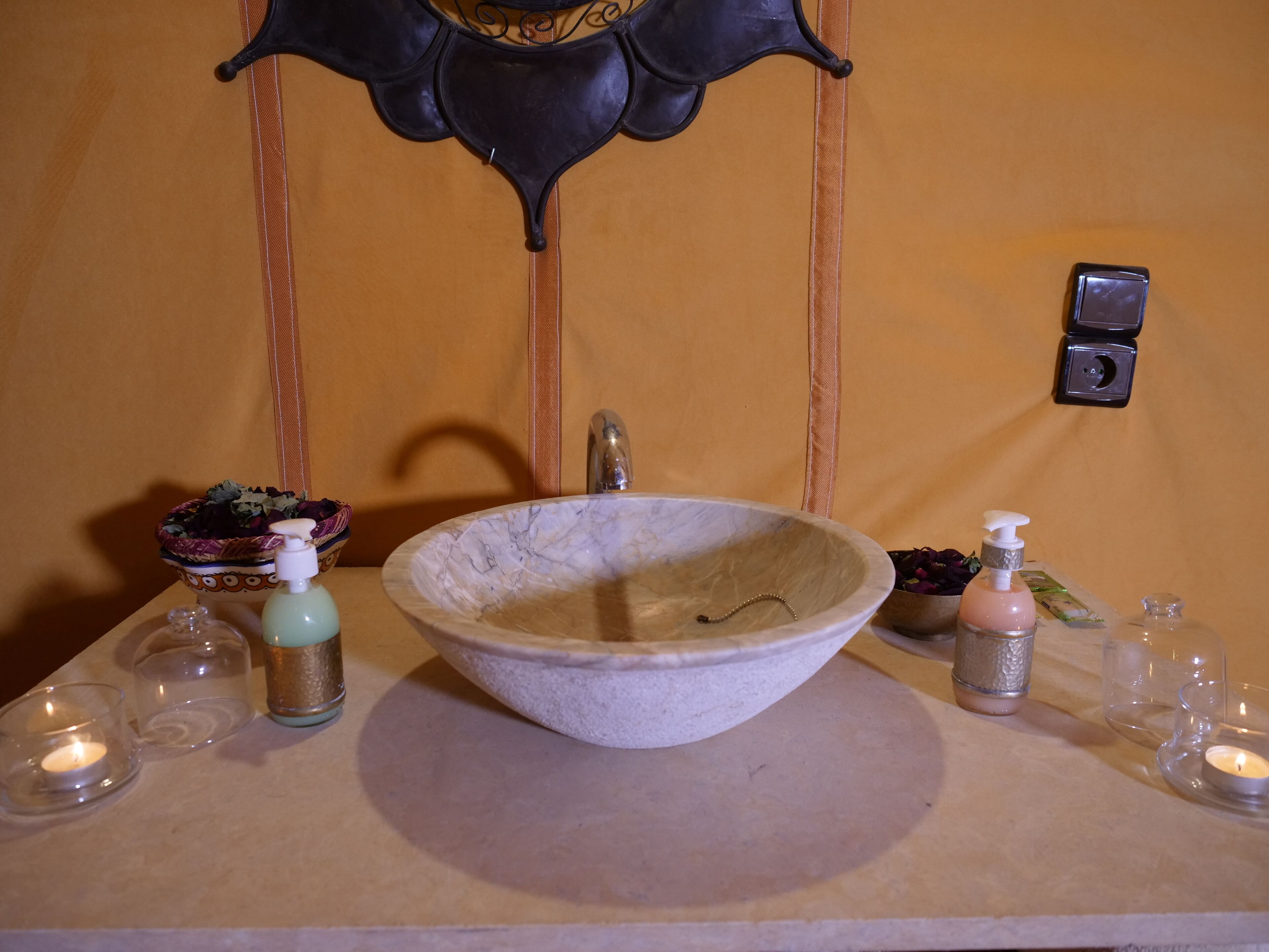 A bathroom with a large marble sink, a decorative mirror, and a wall-mounted light switch.