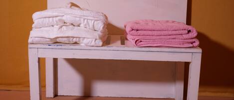A small white bench with two stacks of folded towels, one white and one pink, against a plain wall.