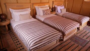 A room with two wooden beds, each with striped bedding and pillows. There are wooden nightstands with lamps and a woven rug on the floor.