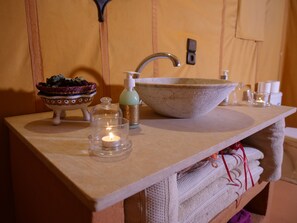 A bathroom with a wooden vanity, a large ceramic sink, a soap dispenser, a candle, and a decorative bowl.