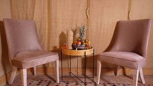 Dos sillas con patas de madera y una mesa de mimbre con frutas y una botella.