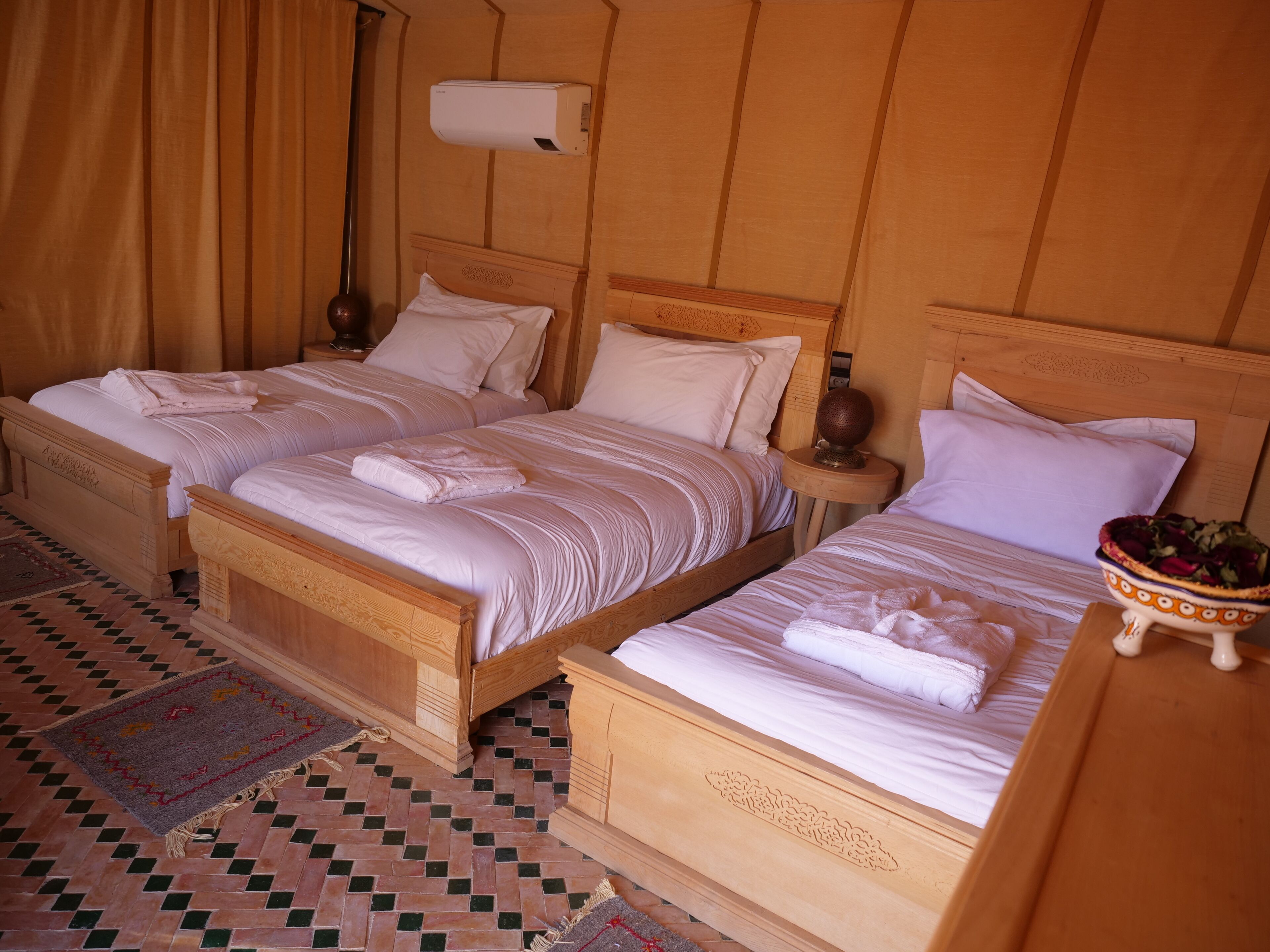 A hotel room with two wooden beds, a wall-mounted air conditioner, and a patterned rug.