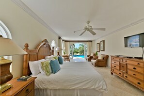 A spacious bedroom with a large bed, a wooden dresser, a desk, and a view of a swimming pool.