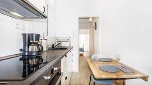 A compact kitchen with a stove, coffee maker, and sink. A dining area with a table and chairs is visible in the background. - Acropolis unique view (Athina)