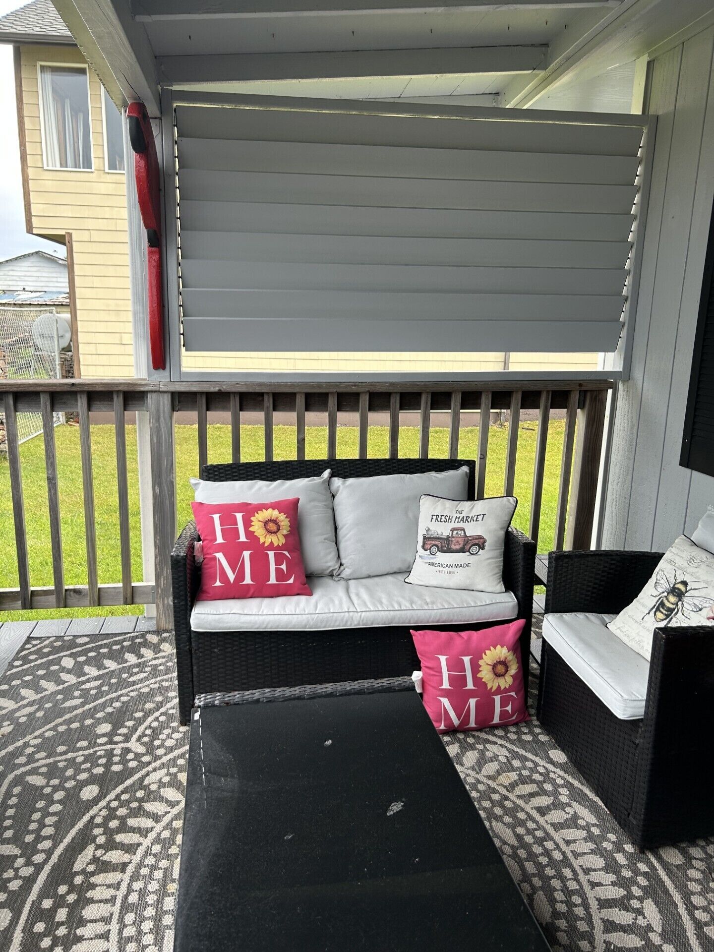 En inglasad veranda med en svart soffa och en tillhörande fåtölj, båda tillverkade av rotting, och dekorerade med kuddar som har solrosor och texten ”HEM” på sig.