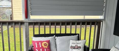 En inglasad veranda med en svart soffa och en tillhörande fåtölj, båda tillverkade av rotting, och dekorerade med kuddar som har solrosor och texten ”HEM” på sig.