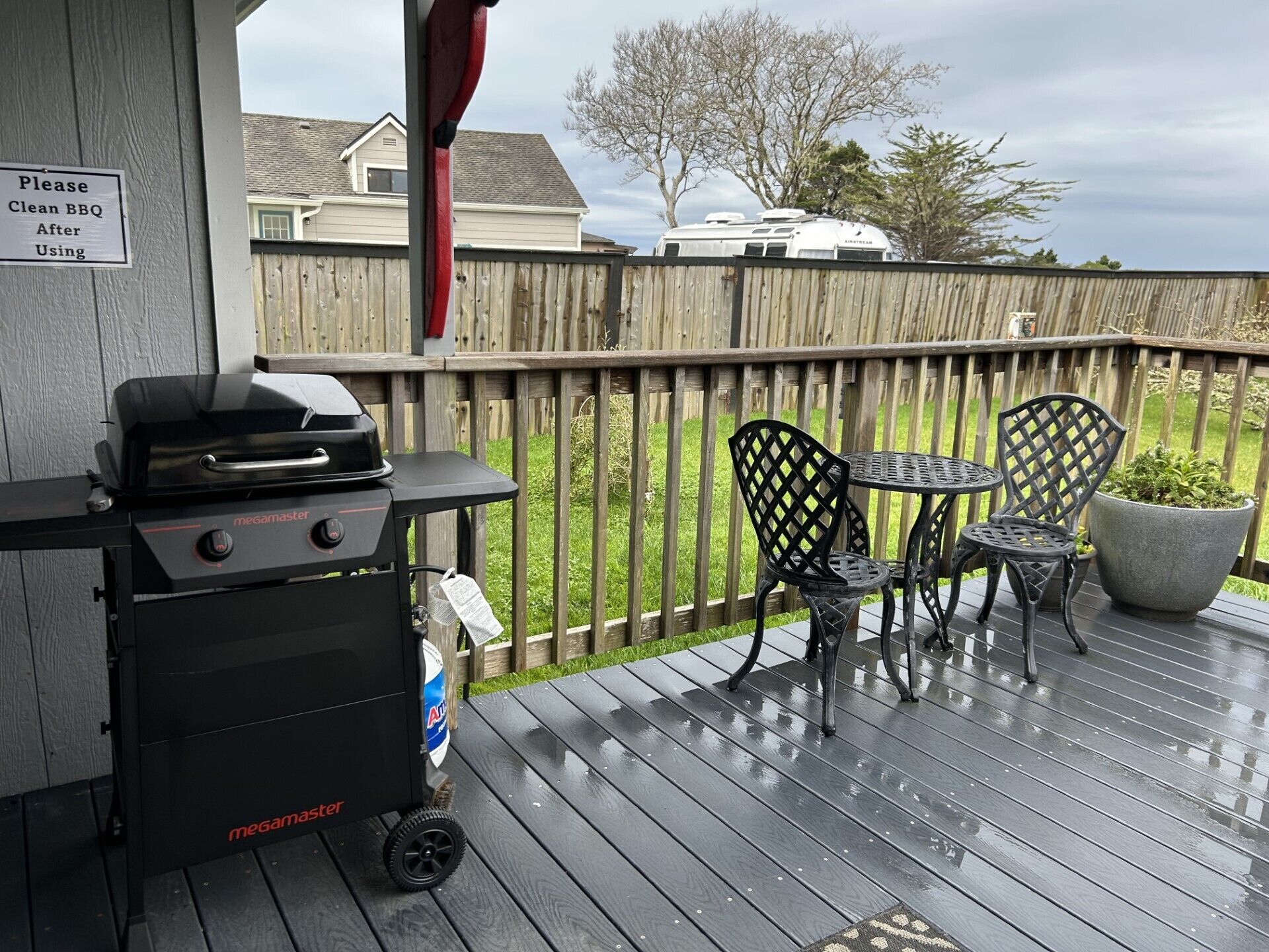 Eine überdachte Terrasse mit einem Megamaster-Grill, Außenmöbeln und einem Schild mit Bitte um Reinigung nach dem Grillen.
